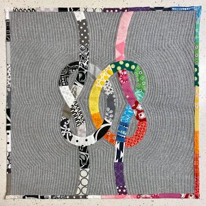 quilt with one black and white knot and one colorful knot intertwined on a gray background