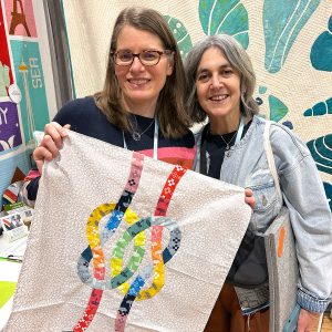 Two women holding a small quilt top of two knots intertwined