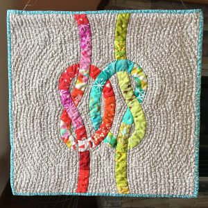 quilt with magenta and aqua / green knots intertwined on a light tan background