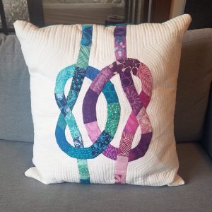 quilted pillow with purple and aqua knots intertwined on a white background