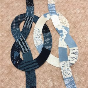 quilt block with dark blue and light blue knots intertwined on a tan background