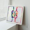 framed quilt of two colorful knots interlocking on a white background next to a window