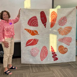 Coral, orange, pink, and sand seashell mini quilt made with the Shoreline Shells quilt pattern.