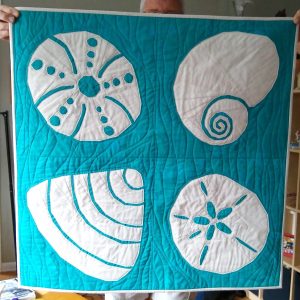 Turquoise, blue, and sand seashell mini quilt made with the Shoreline Shells quilt pattern.