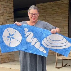 Light blue and cream seashell quilt blocks, held by a woman, made with the Shoreline Shells Block of the Month pattern.