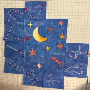 zodiac constellations, stars, and moon quilt blocks and cut fabric on a design wall in a quilting room