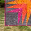 detail of the lower left corner of a modern, colorful quilt with grass in the background