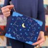 woman holding a zippered pouch with a star filled night sky, moon, and zodiac constellations