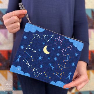 woman holding a zippered pouch with a star filled night sky, moon, and zodiac constellations