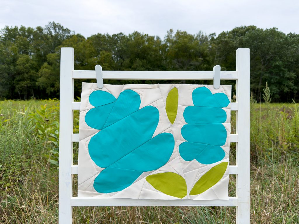 quilt block with blue flowers and green leaves on a ladder in a field
