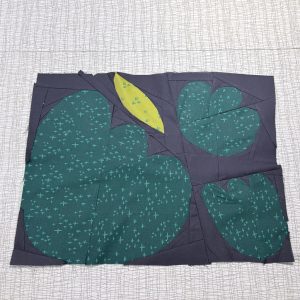 flower and leaf quilt block with turquoise blender fabric, bright green fabric on a dark blue backgrouns