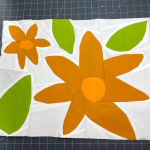 Modern floral quilt block in muted orange and bright green with a white background on a cutting mat