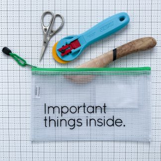 Translucent waterproof vinyl project bag with “Important Things Inside” printed on the front and scissors, a rotary cutter, and wooden hera marker