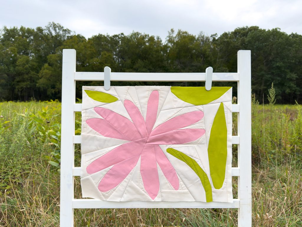 quilt block with pink flower and green leaves on a ladder in a field