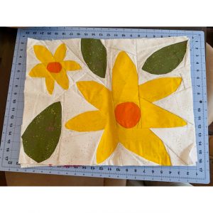 quilt block of large yellow and orange flowers and leaves on a cutting mat