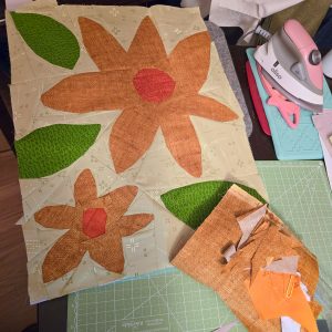 quilt block of large yellow and orange flowers and leaves sitting on a work table