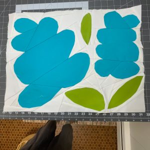 large foundation paper pieced flower quilt block with blue, green, and white fabric on cutting mat