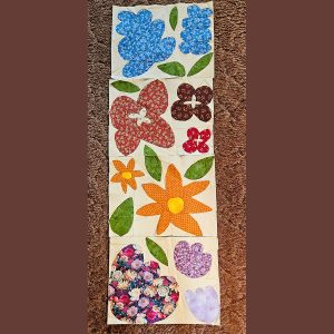 row of colorful flower quilt blocks made with floral fabric and scraps of white fabric on top of a carpet