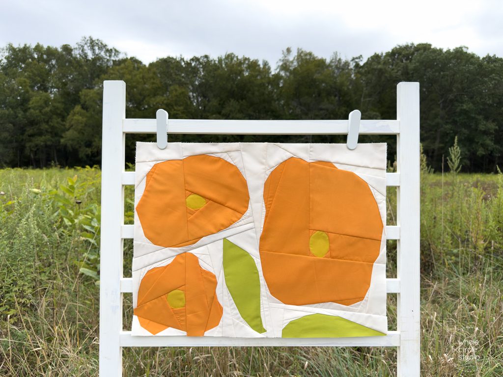 quilt block with orange flowers and green leaves on a ladder in a field