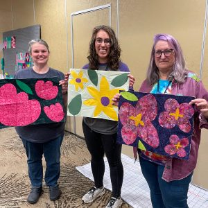 3 women holding flower quilt blocks