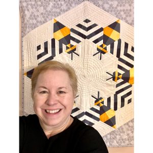 smiling woman in front of a bee themed modern quilt