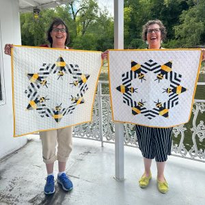 two smiling women holding bee quilts