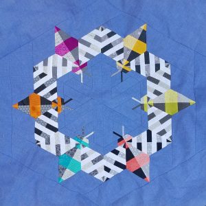 Bright modern quilt featuring pieced bees made from colorful fabrics on a blue background