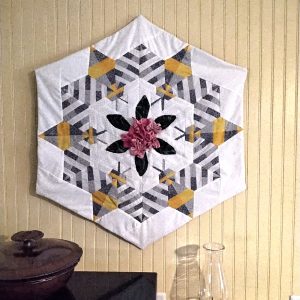 Modern wall hanging quilt featuring large stylized bees and a 3 dimensional fabric flower in the middle