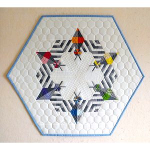 Bright modern quilt featuring pieced bees made from colorful fabrics in a hexagon shape with a blue binding