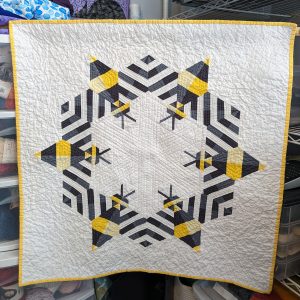 Modern bee quilt with graphic yellow, gray, and black bee blocks arranged on a light background.