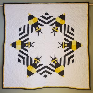 Modern bee quilt with graphic yellow, gray, and black bee blocks arranged on a light background.