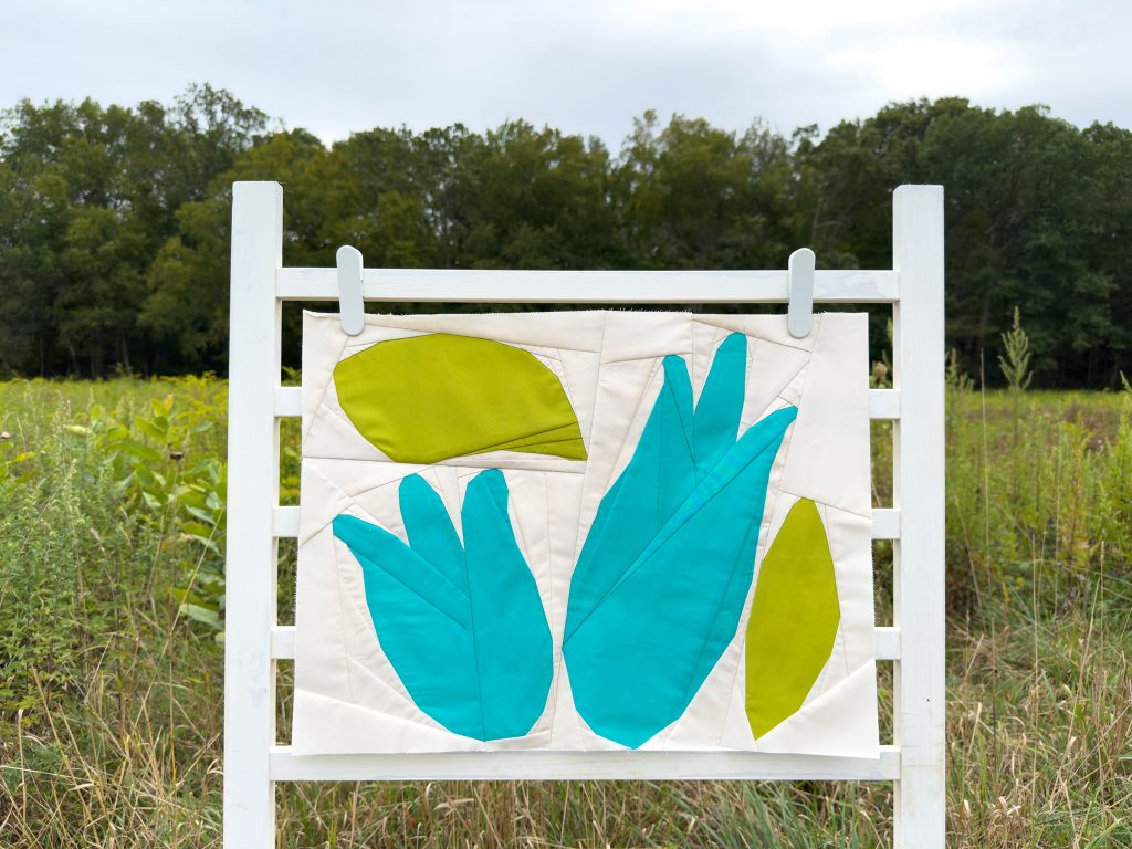 modern quilt block with blue flowers and green leaves on a ladder in a field