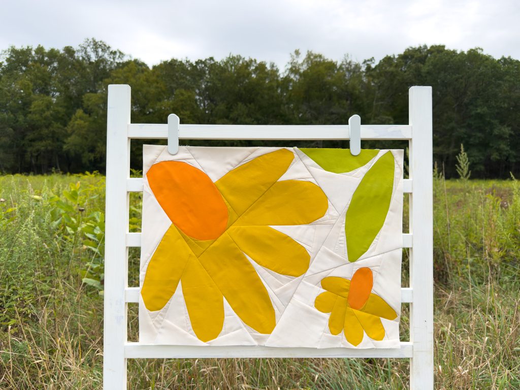 modern quilt block with yellow and orange flowers and green leaves on a ladder in a field