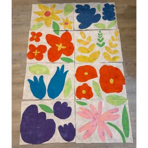 Multiple colorful flower quilt blocks arranged on a floor before being assembled into a quilt.
