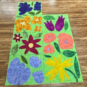 Bright fabric flower quilt blocks arranged on a wood floor while a quilt is in progress.