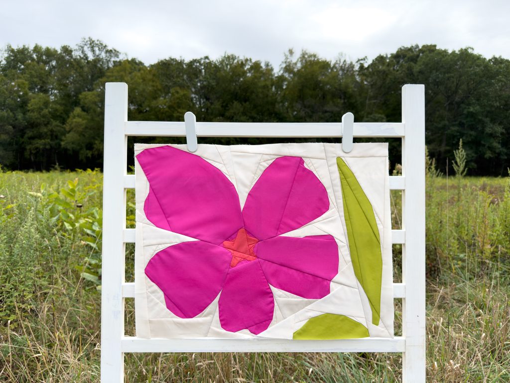 modern quilt block with magenta flower and green leaves on a ladder in a field